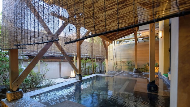 Un onsen japonés tradicional con estructura de madera, asientos de piedra y una piscina de agua cristalina.