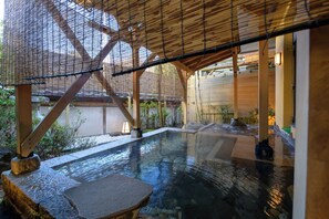 A traditional Japanese onsen with a wooden structure, stone seating, and a clear water pool. - Tamaya Ryokan (Ueda)