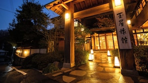 Entrada de una construcción tradicional japonesa, con estructura de madera y escalones de piedra que conducen a un portón.