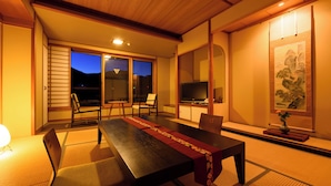 Una habitación tradicional japonesa con suelo de tatami, una mesa baja con un corredor rojo y una puerta corrediza que da a un balcón.