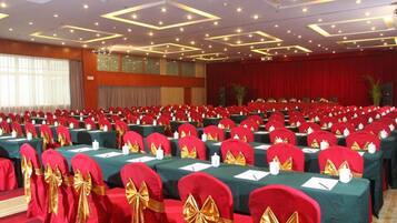 A conference room with rows of tables, red chairs with gold sashes, and a stage with a red curtain.
