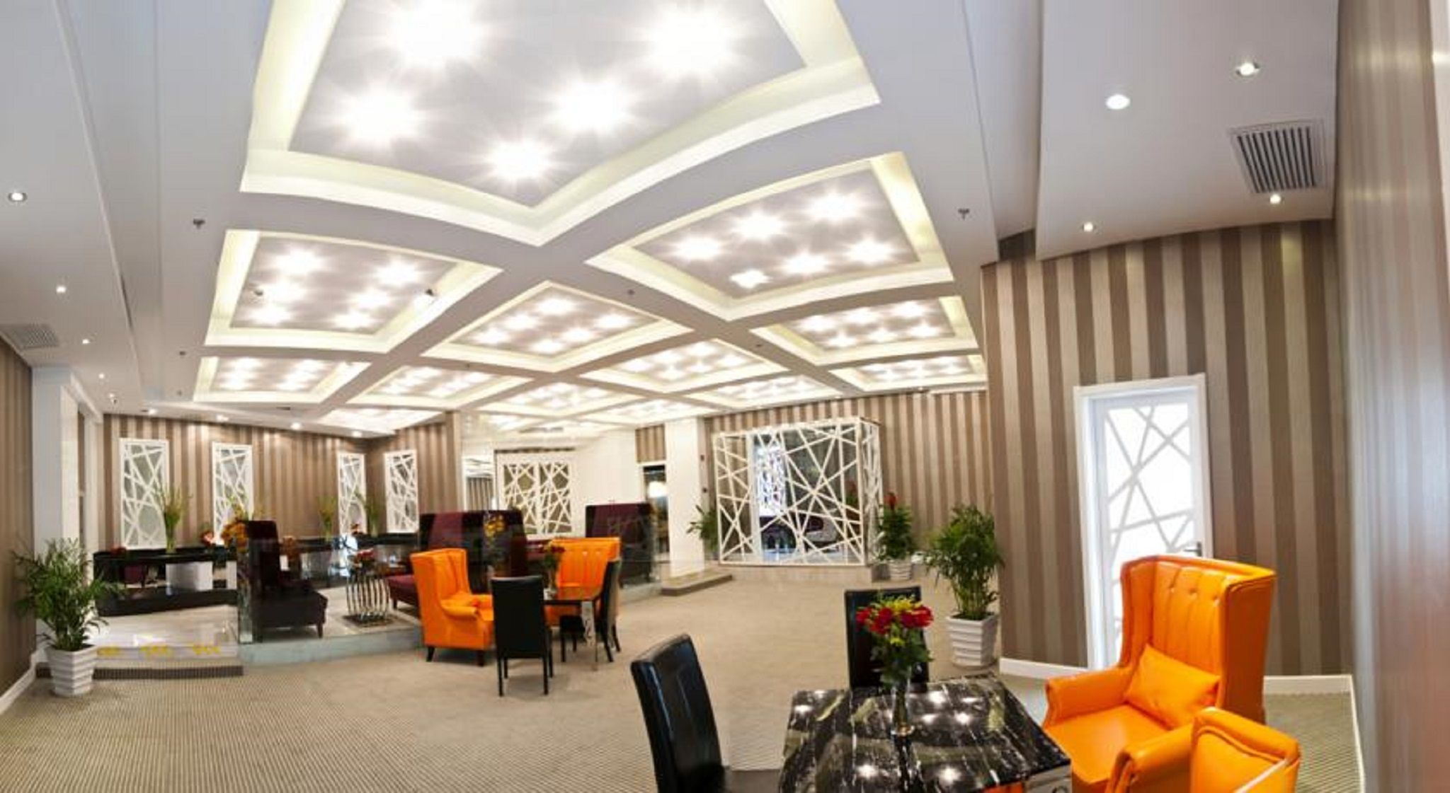 A hotel lobby with a modern ceiling design, seating areas, and decorative elements.