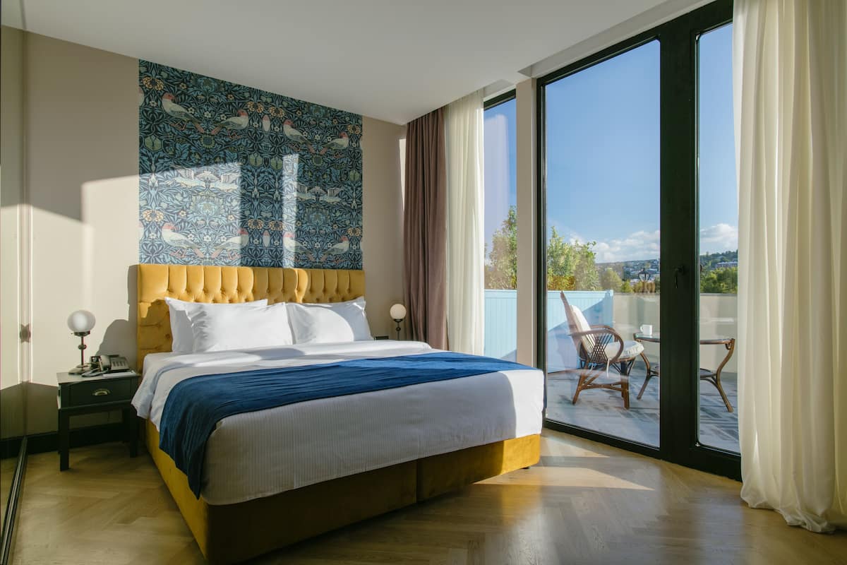 Un dormitorio con una cama grande, una mesita de noche, un tapiz en la pared y vistas al exterior a través de un ventanal corredero.