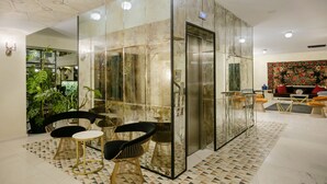 A modern lobby with a glass elevator, seating area with round tables and chairs, and a patterned floor. - Museum Hotel Orbeliani (Tbilisi)