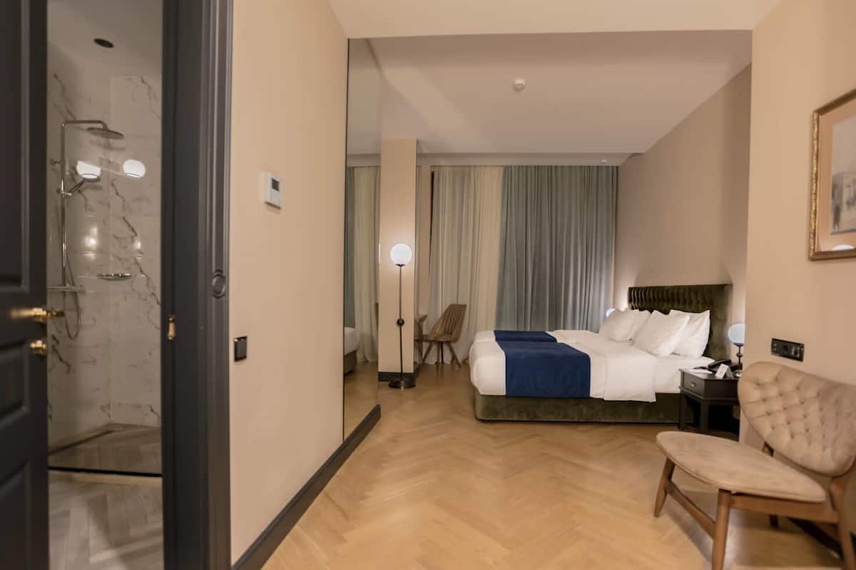 Habitación de hotel con cama, una silla, escritorio, lámpara y zona de ducha.