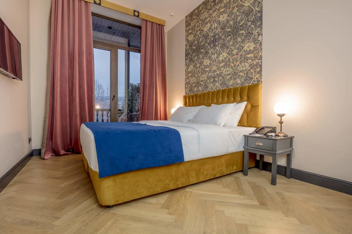 Una habitación de hotel con cama, mesita de noche, pared con diseño y ventana con cortinas.