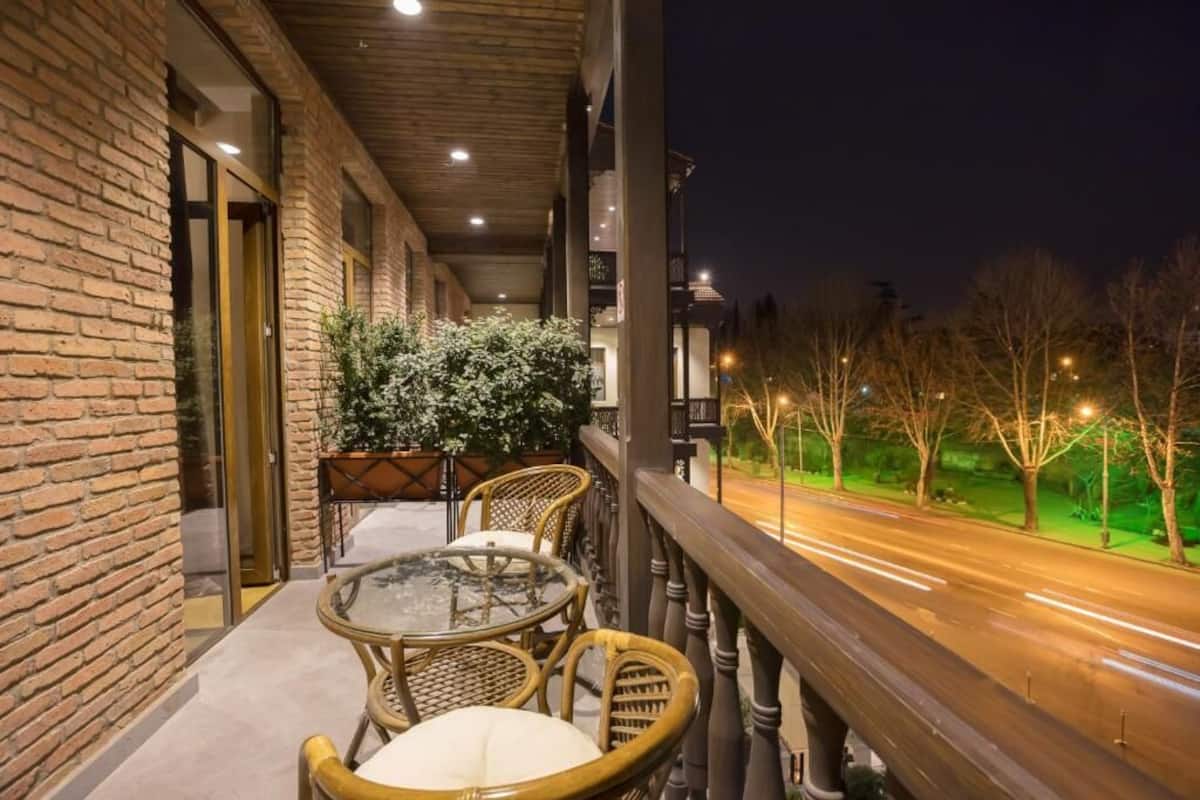 Un balcón con mobiliario de mimbre, una mesa de vidrio y vista a una carretera por la noche.