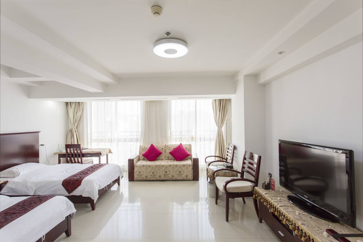 A hotel room with two beds, a sofa, a TV, and a dining area.