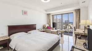 A hotel room with a large bed, a desk with a chair, a TV, and a view of the city through a large window. - Sanya Huabaoshi Hotel (Sanya)