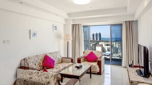 A modern living room with two sofas, a coffee table, and a TV. The room has a large window with a city view. - Sanya Huabaoshi Hotel (Sanya)
