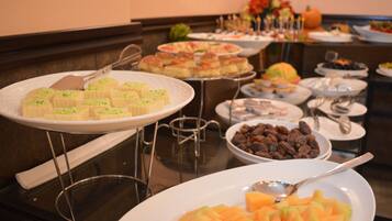 A buffet with various dishes including pastries, fruits, and nuts.