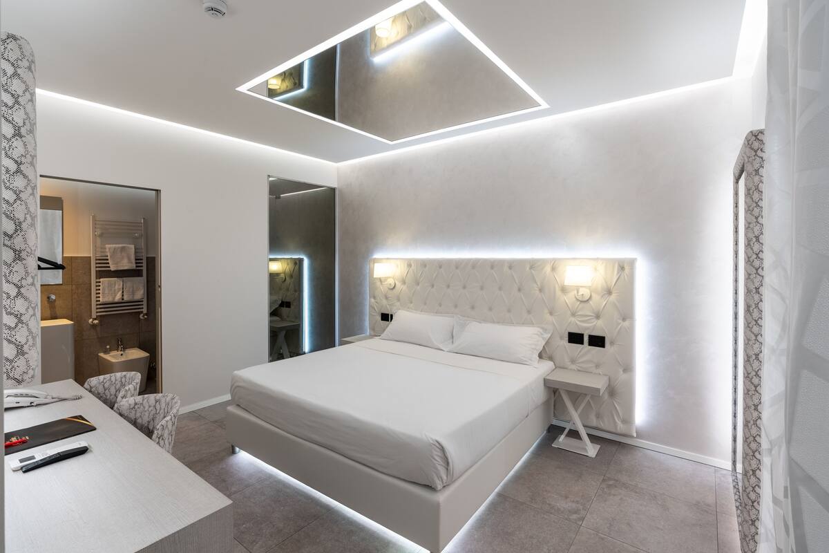 Une chambre d’hôtel moderne avec un grand lit, des tables de chevet, un bureau et un miroir.