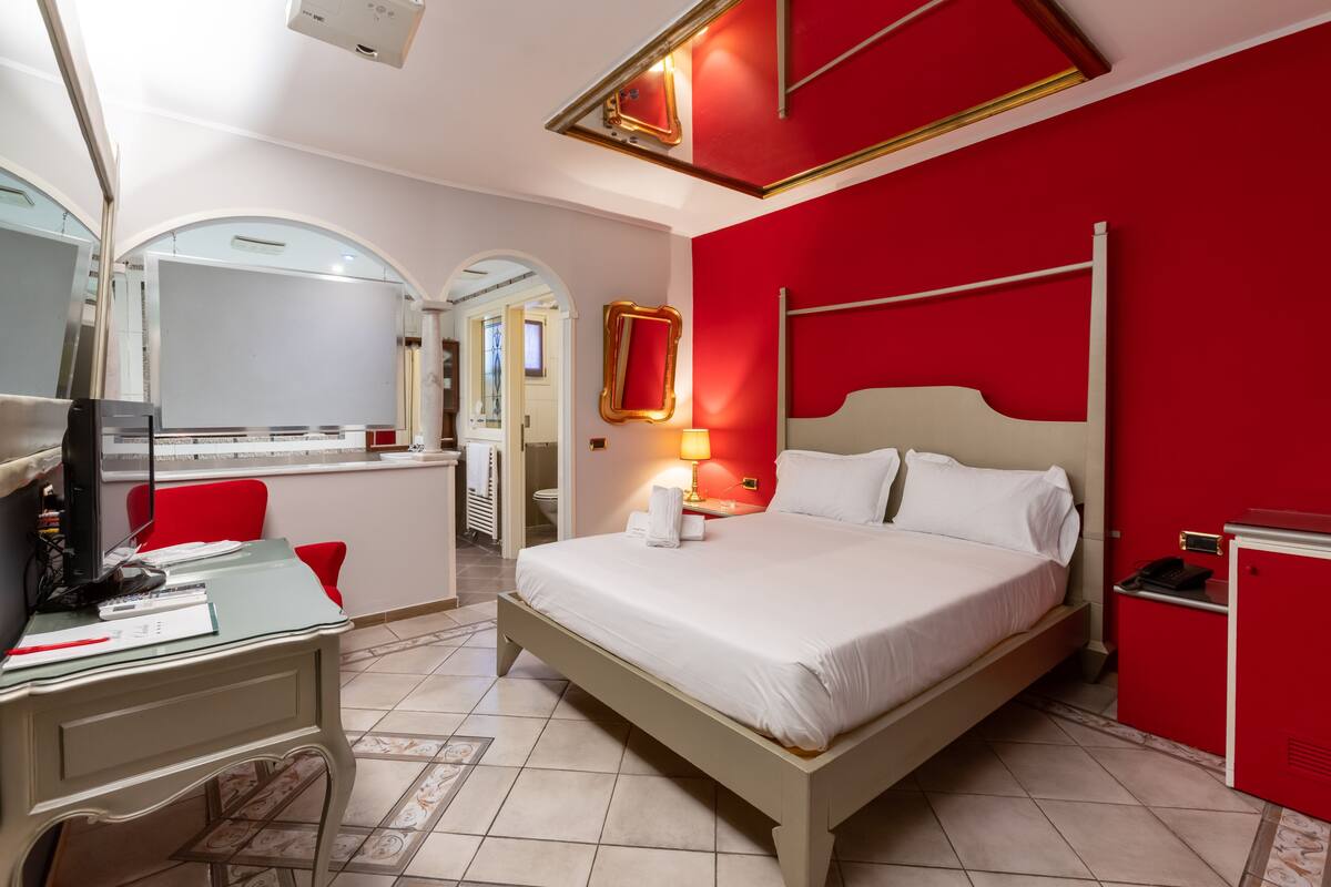 Une chambre d’hôtel avec un lit, un bureau et un mur d’accent de couleur rouge.