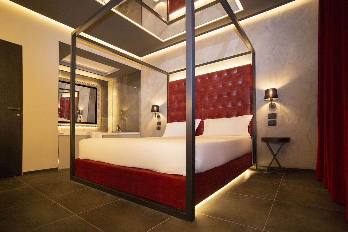 Une chambre d’hôtel moderne avec un lit à baldaquin, un grand miroir, une petite table d’appoint et un rideau rouge.