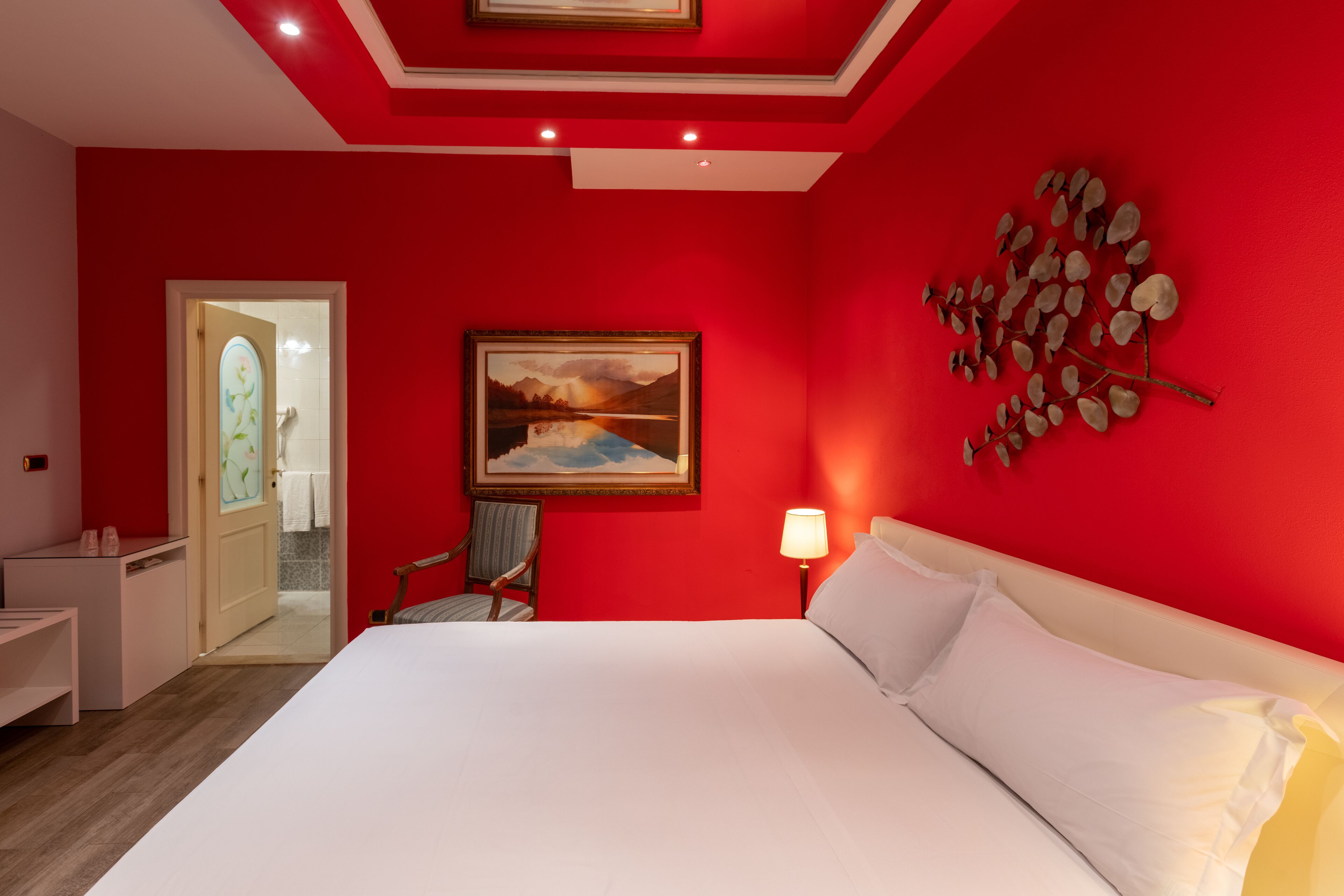 A hotel room with a large bed, a painting on the wall, a chair, and a desk.