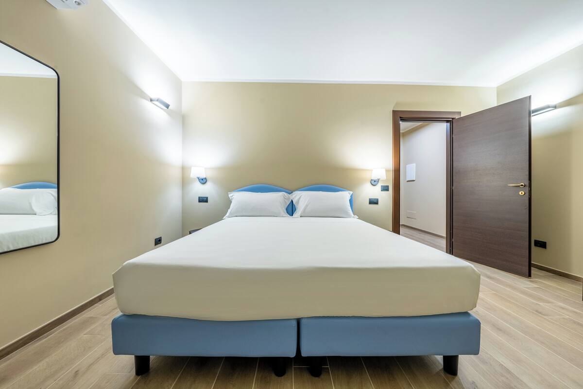 Une chambre à coucher avec un grand lit, deux tables de chevet, un miroir et une porte.