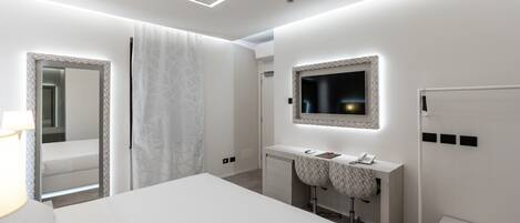 A modern hotel room with a large bed, a vanity with a mirror, a desk, and a television.