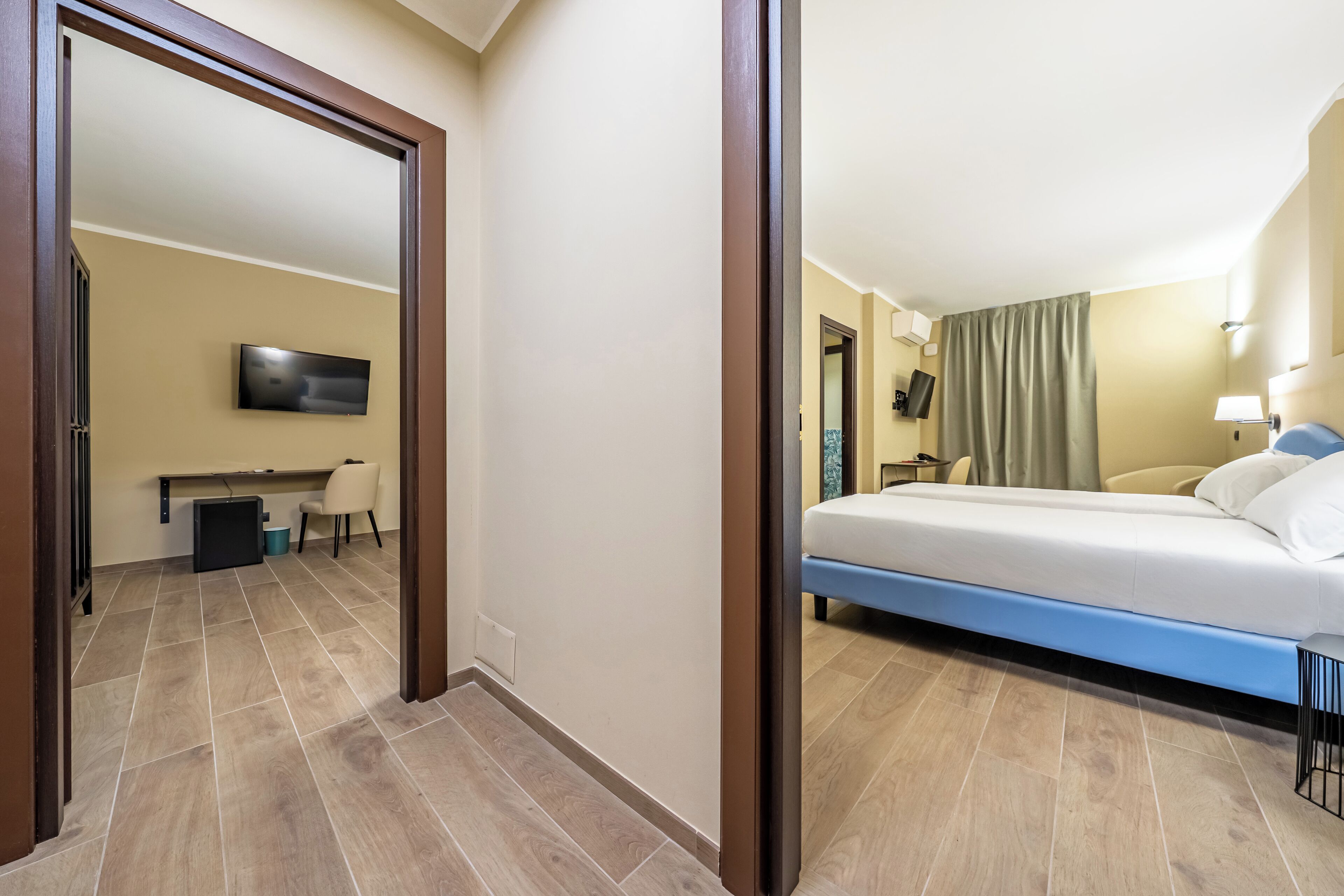 A hotel room with a bed, a desk with a chair, and a television on the wall.