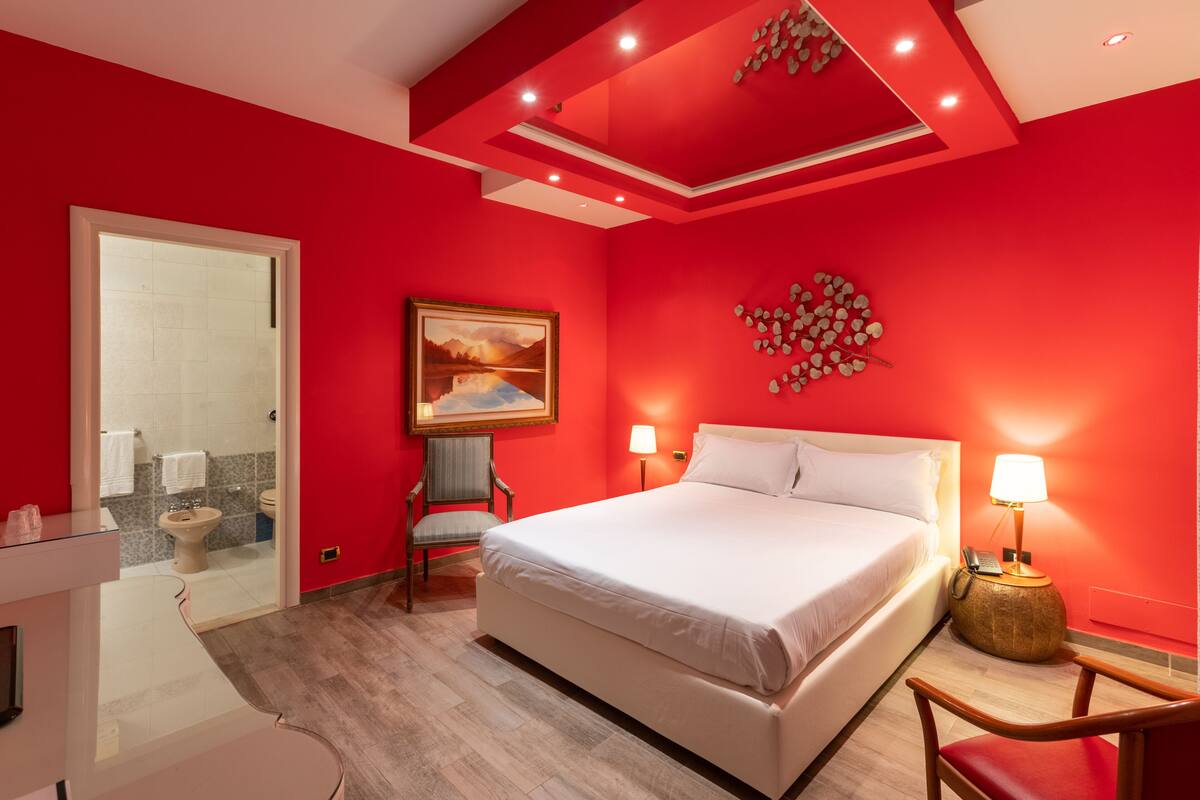 Une chambre d’hôtel avec un grand lit, une chaise, un bureau et une salle de bain visible à travers une porte ouverte.