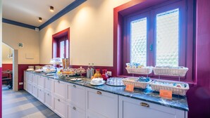 A breakfast bar with various food items and baskets, a window with a view, and a door with a red frame. - CHARLIE HOTEL Charme & Comfort (Settala)