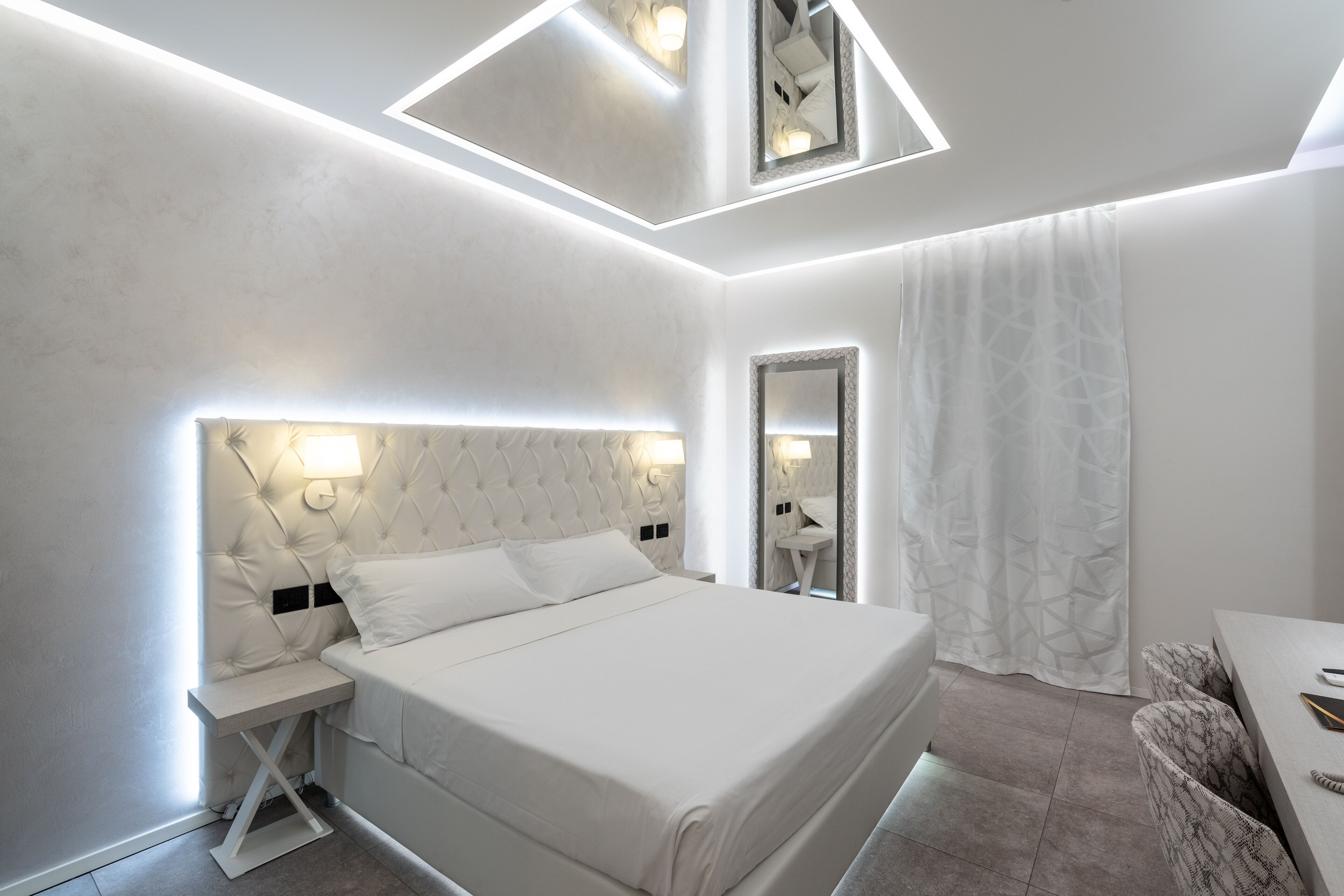 A modern bedroom with a large bed, bedside tables, a mirror, and a desk.