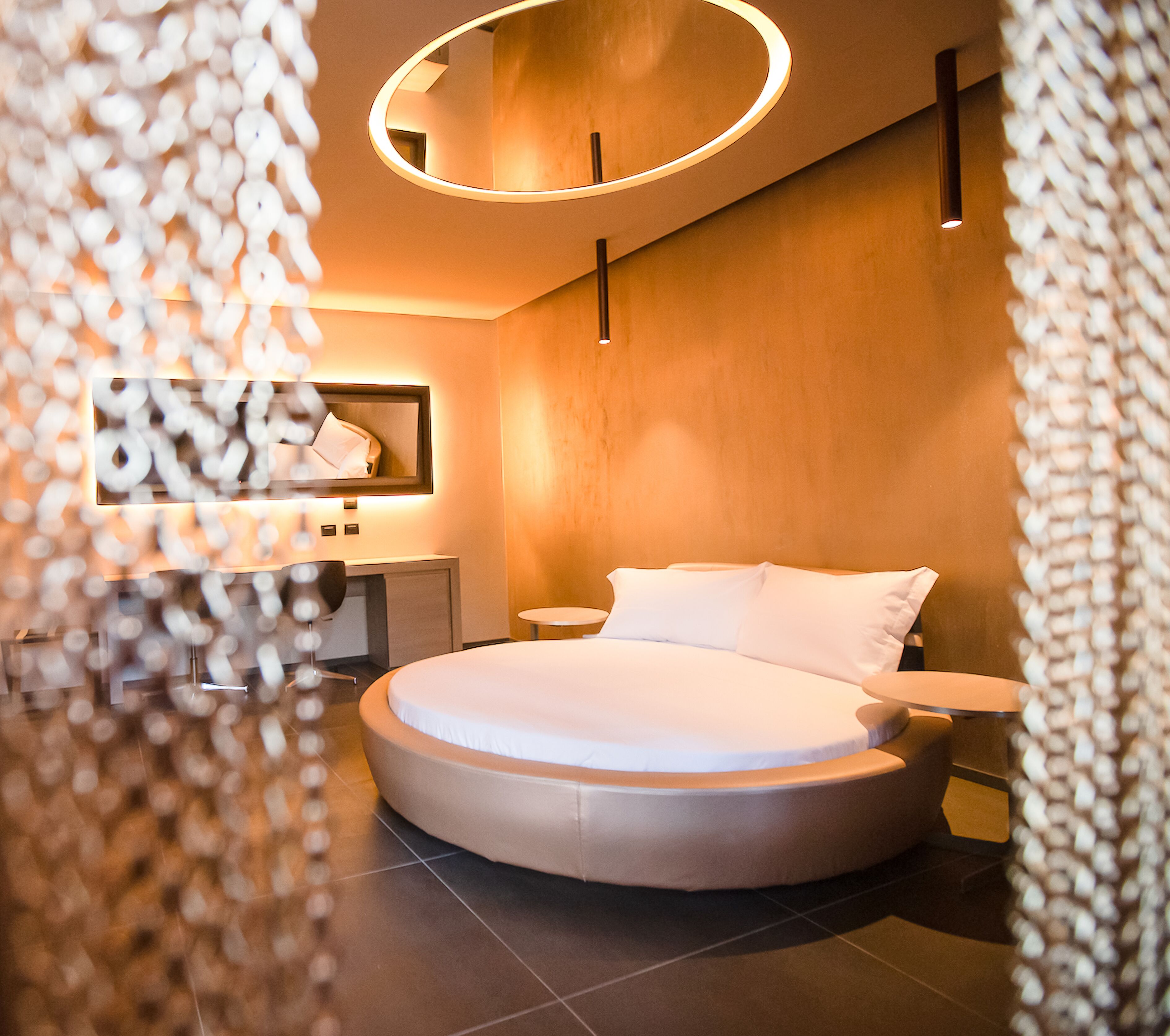 A modern bedroom with a circular bed, a round mirror, a bedside table, and a nightstand.