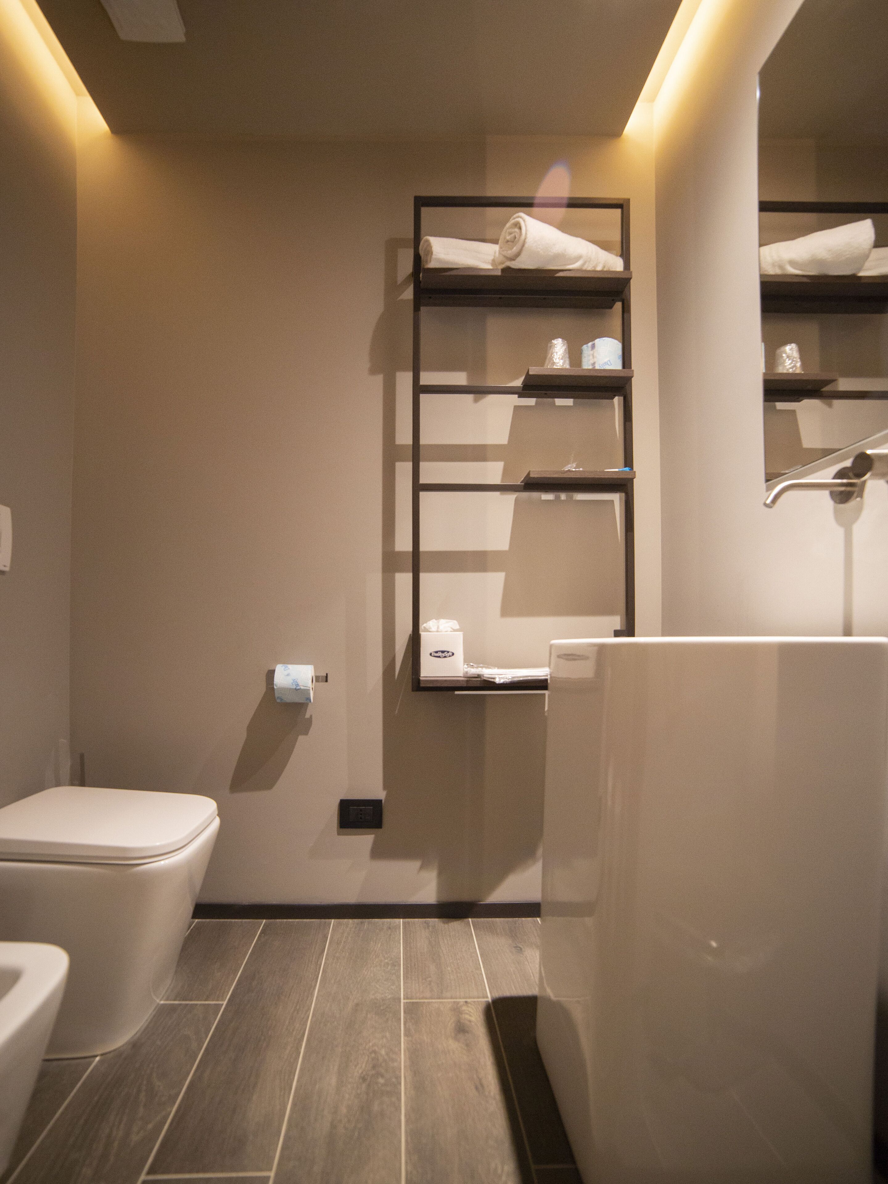 A modern bathroom with a toilet, a sink, and a mirror with shelves above.