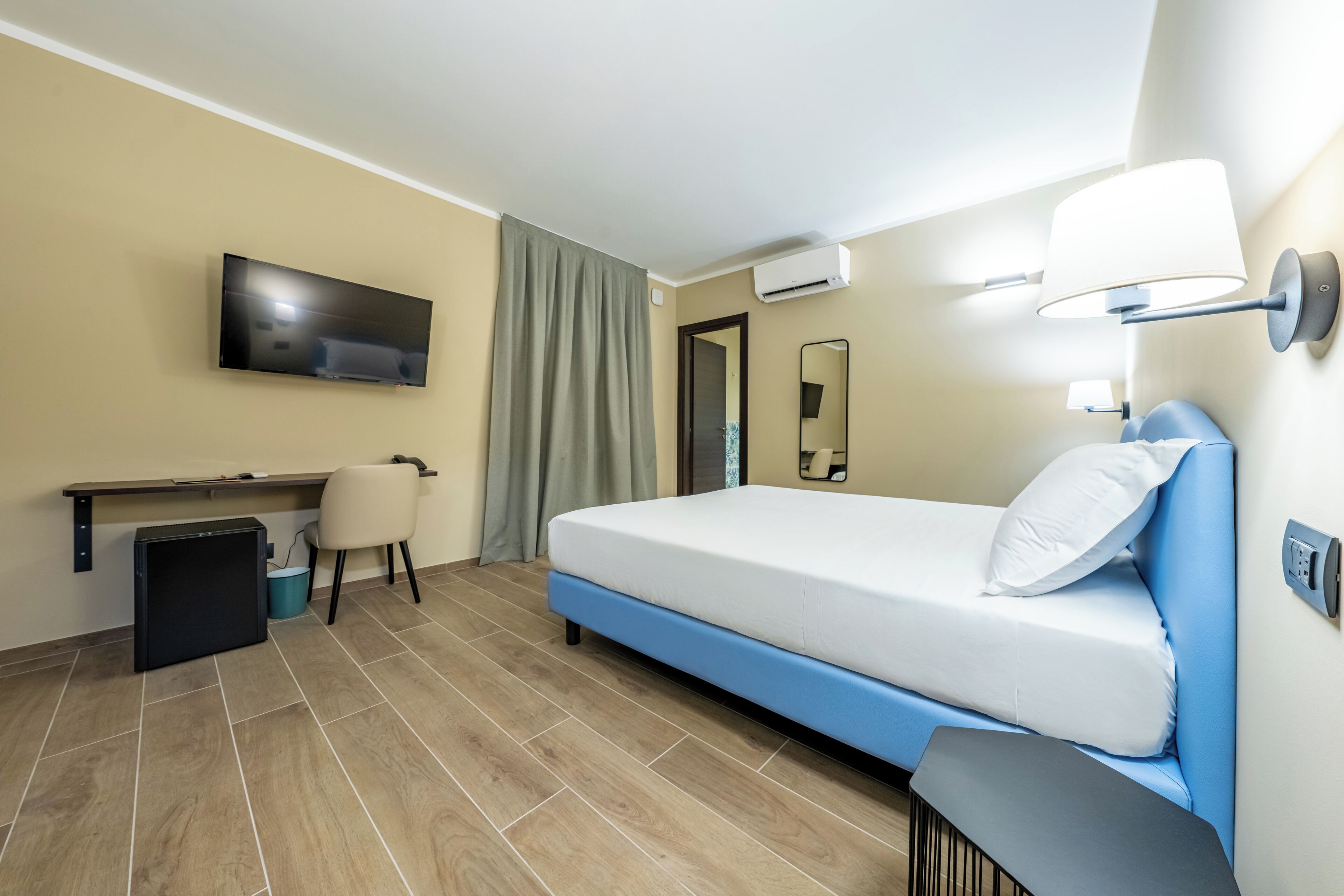 Ein Hotelzimmer mit Bett, Schreibtisch, Stuhl, Fernseher, Klimaanlage und einer Wandlampe.