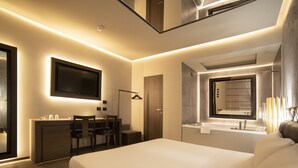 A modern hotel room with a large bed, a desk with a chair, a flat-screen TV mounted on the wall, and a bathroom with a large mirror and sink. - CHARLIE HOTEL Charme & Comfort (Settala)