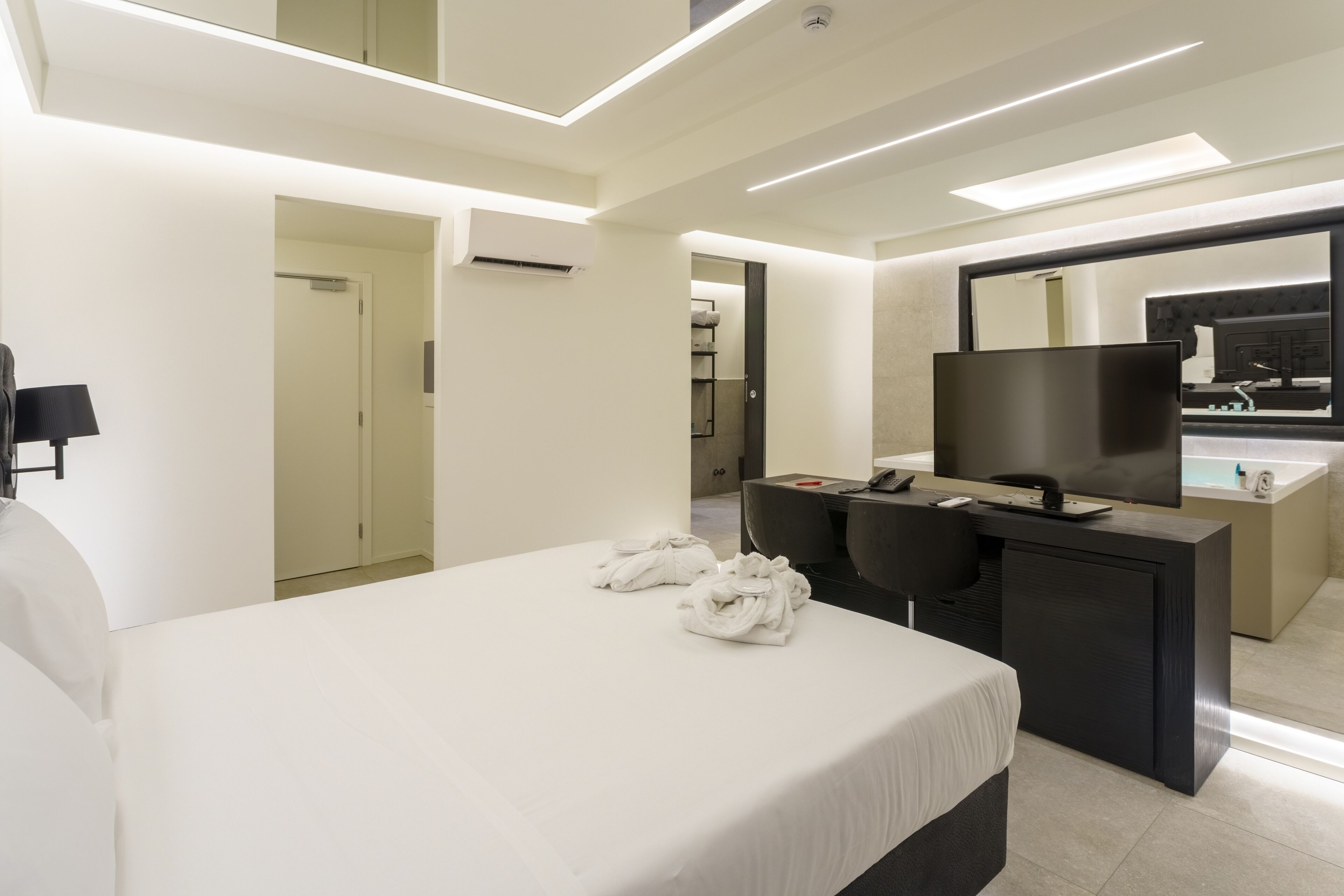 A modern hotel room with a large bed, a desk with a flat-screen TV, and a bathroom with a bathtub.
