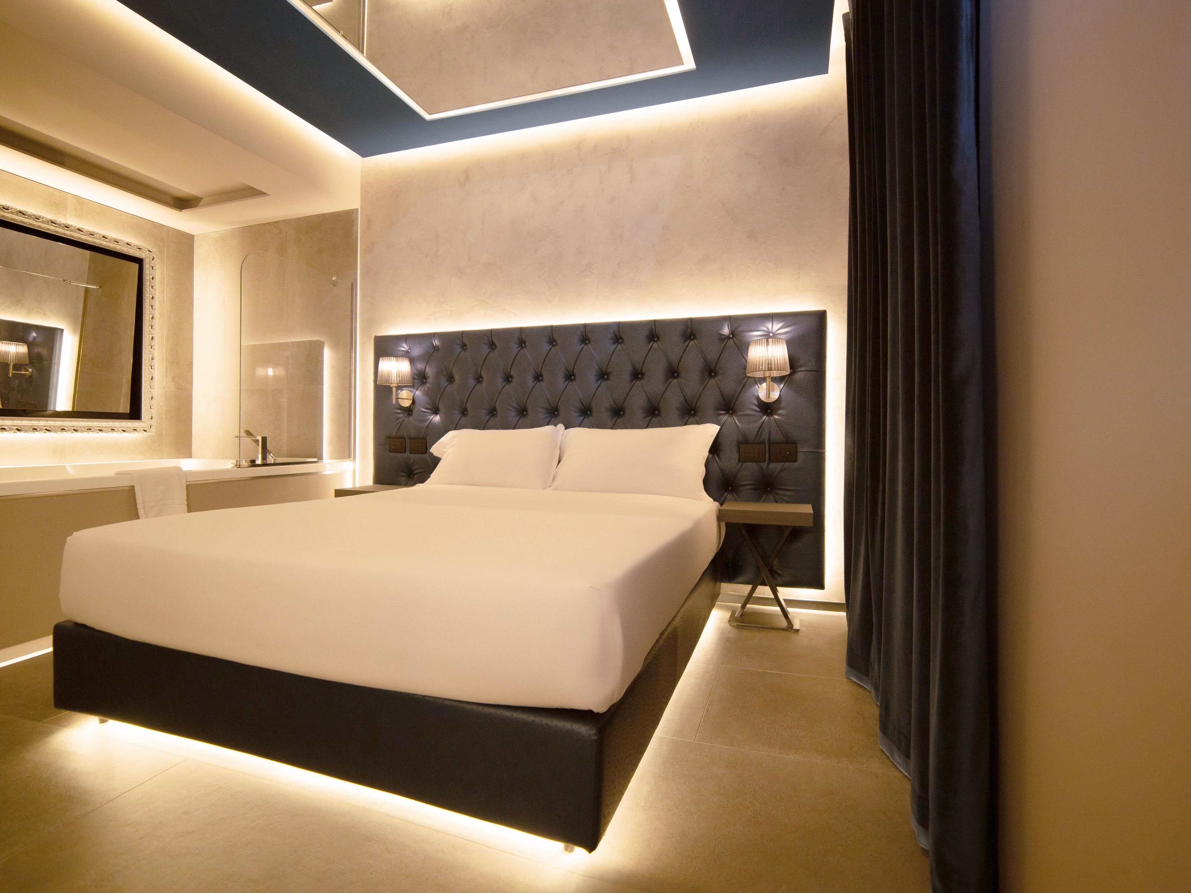 A modern hotel room with a large bed, a nightstand with a lamp, and a mirror above the bed.