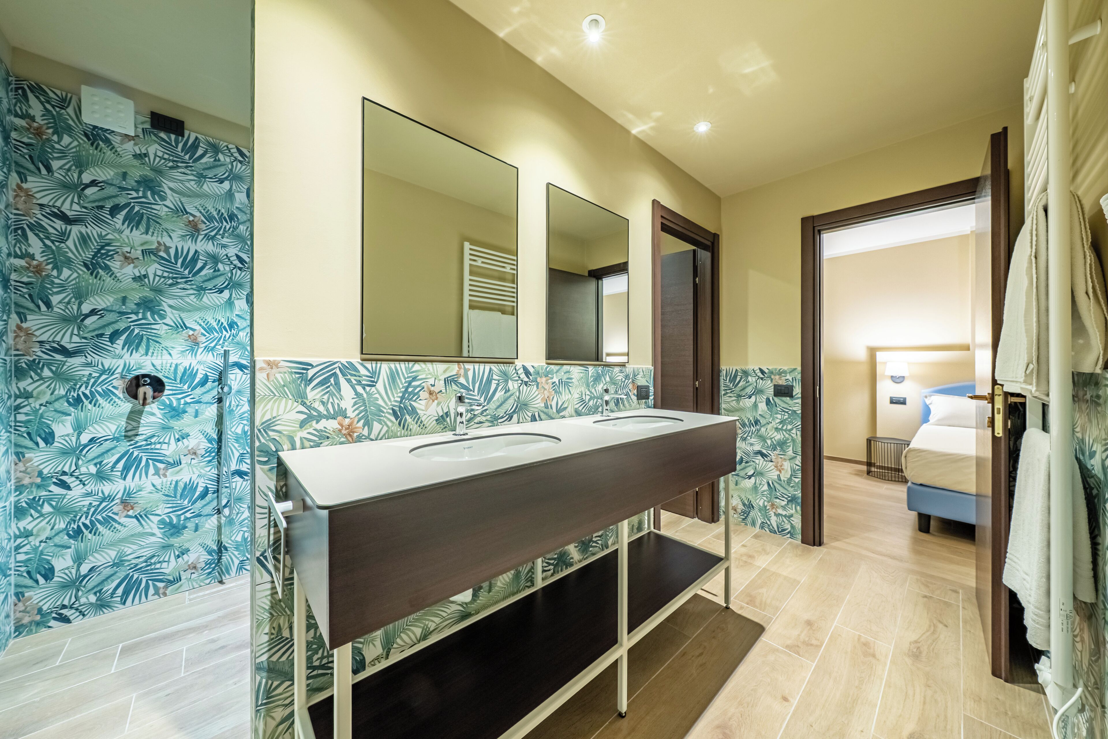 A bathroom with a double sink vanity, a large mirror, and a shower area with a tropical leaf pattern.