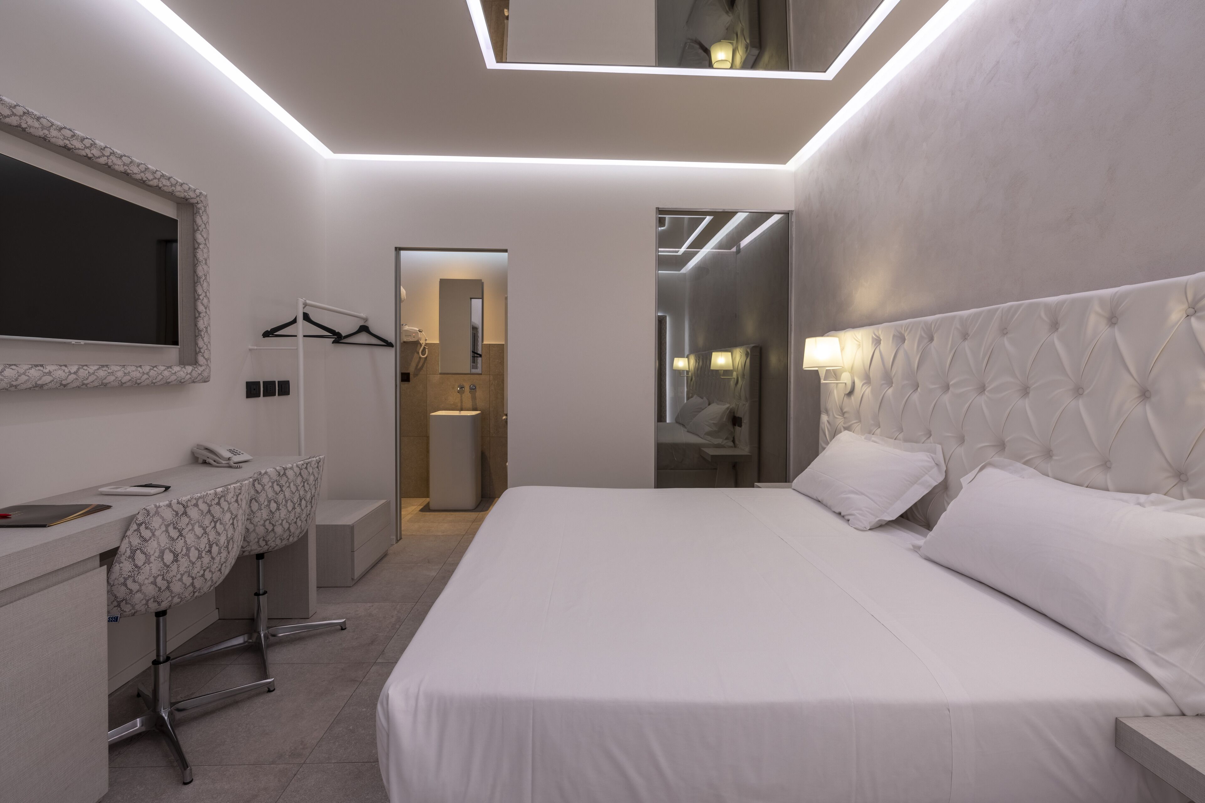 Ein modernes Hotelzimmer mit einem großen Bett, einem Schreibtisch mit Stuhl, einem Spiegel und einem begehbaren Kleiderschrank.
