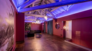 A spacious lobby with a high ceiling, exposed wooden beams, a seating area with a sofa and a small table, and a mural on the left wall. - CHARLIE HOTEL Charme & Comfort (Settala)