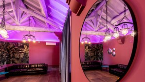 A room with a wooden ceiling, a large mirror, a black leather sofa, and a tropical wallpaper. - CHARLIE HOTEL Charme & Comfort (Settala)