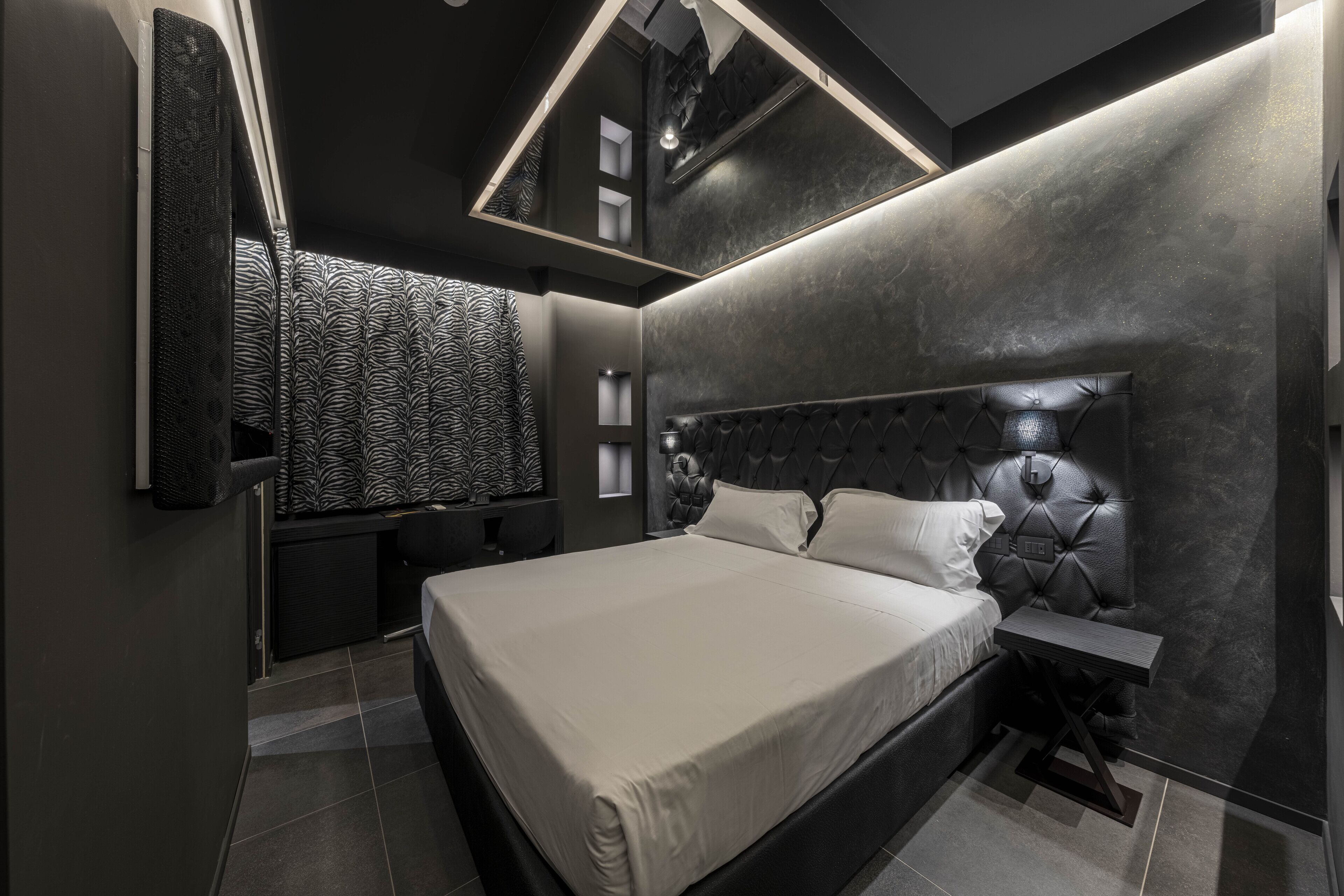 Une chambre moderne avec un grand lit, une tête de lit dotée d’un éclairage intégré, une table de chevet et un mur orné d’un motif.