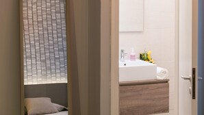 A bedroom with a bed, a bedside table, a mirror, and a door leading to a bathroom with a sink and towel. - Hotel La Diga - Altomincio Family Park (Valeggio sul Mincio)