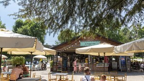 An outdoor seating area with tables and chairs under umbrellas, a bar in the background, and a sign for 'froggy's bar'. - Hotel La Diga - Altomincio Family Park (Valeggio sul Mincio)