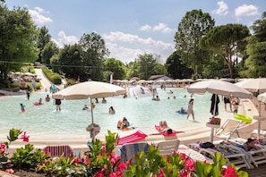 A swimming pool area with multiple umbrellas, lounge chairs, and people swimming and relaxing. - Hotel La Diga - Altomincio Family Park (Valeggio sul Mincio)