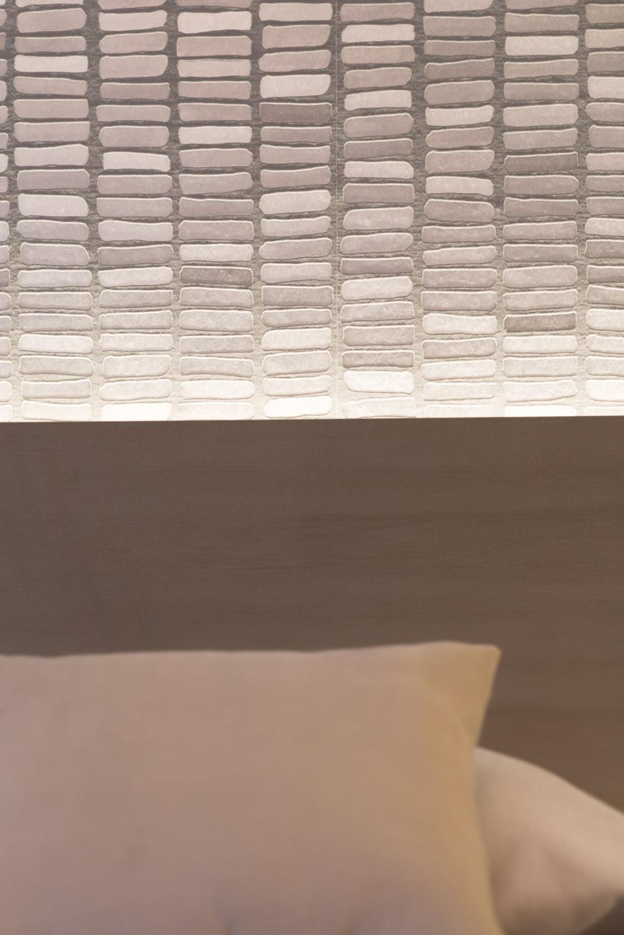 A window with a textured pattern, a white pillow, and a brown wall.