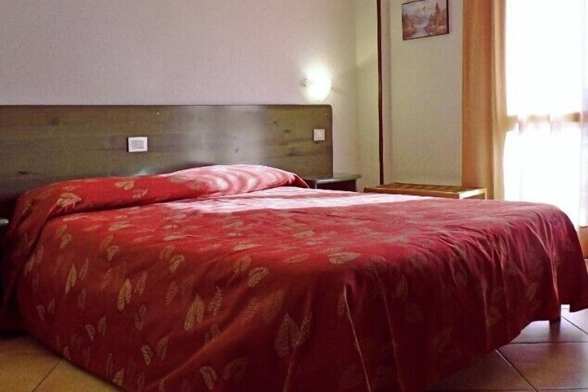 A hotel room with a large bed, a headboard, a nightstand, a wall-mounted light, and a window with curtains.