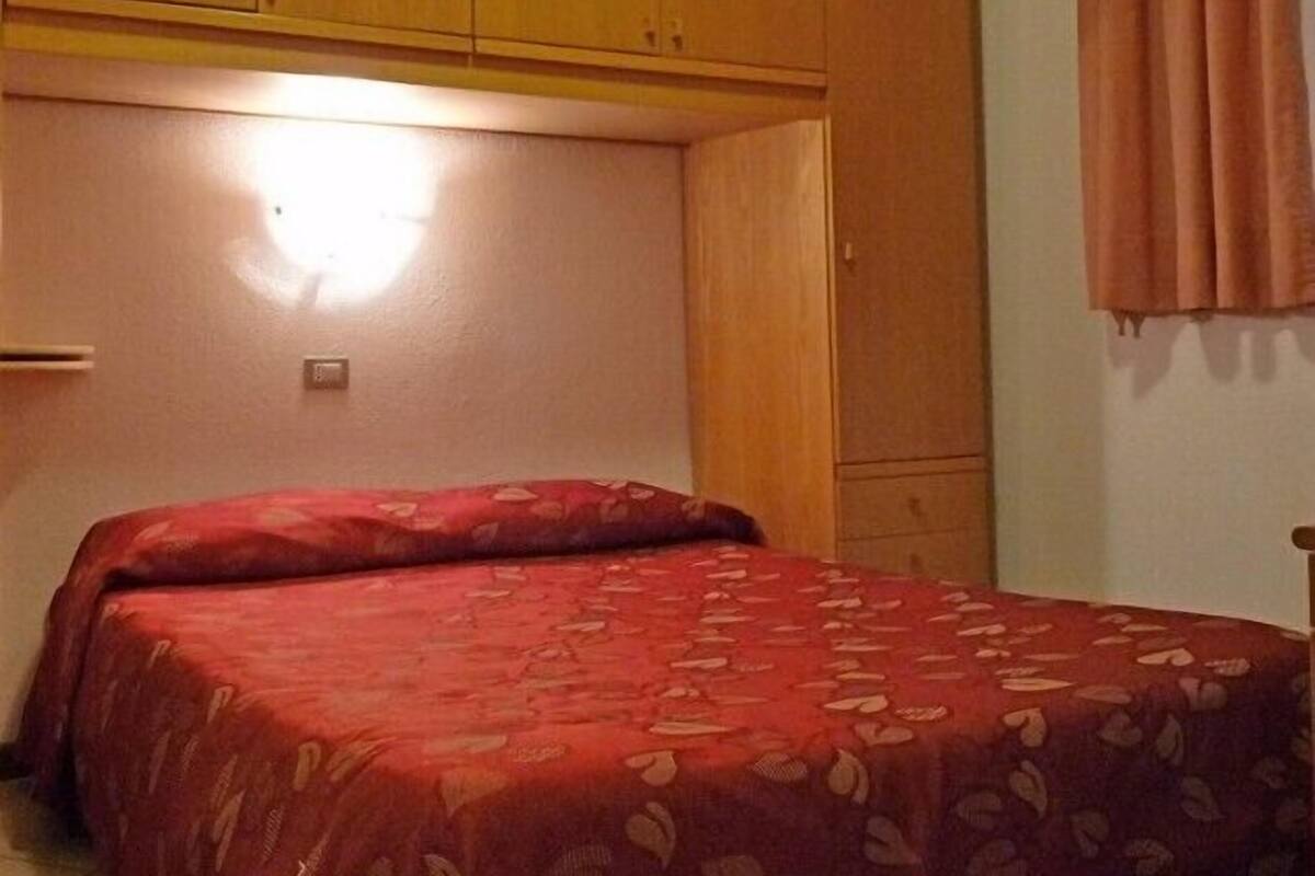 A bedroom with a bed, wooden wardrobe, and a window with curtains.