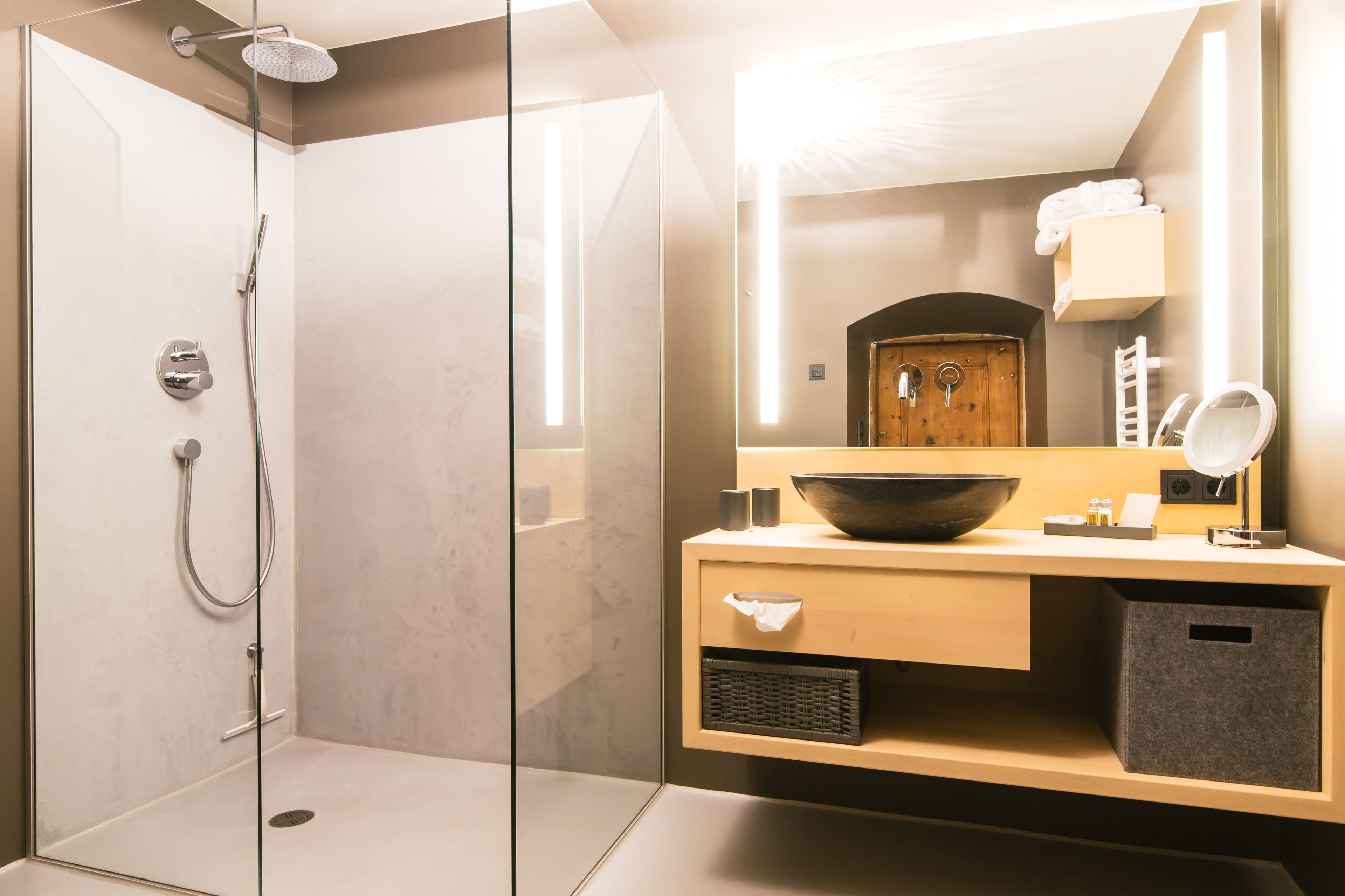 A modern bathroom with a glass-enclosed shower, a wooden vanity with a large sink, and a mirror.