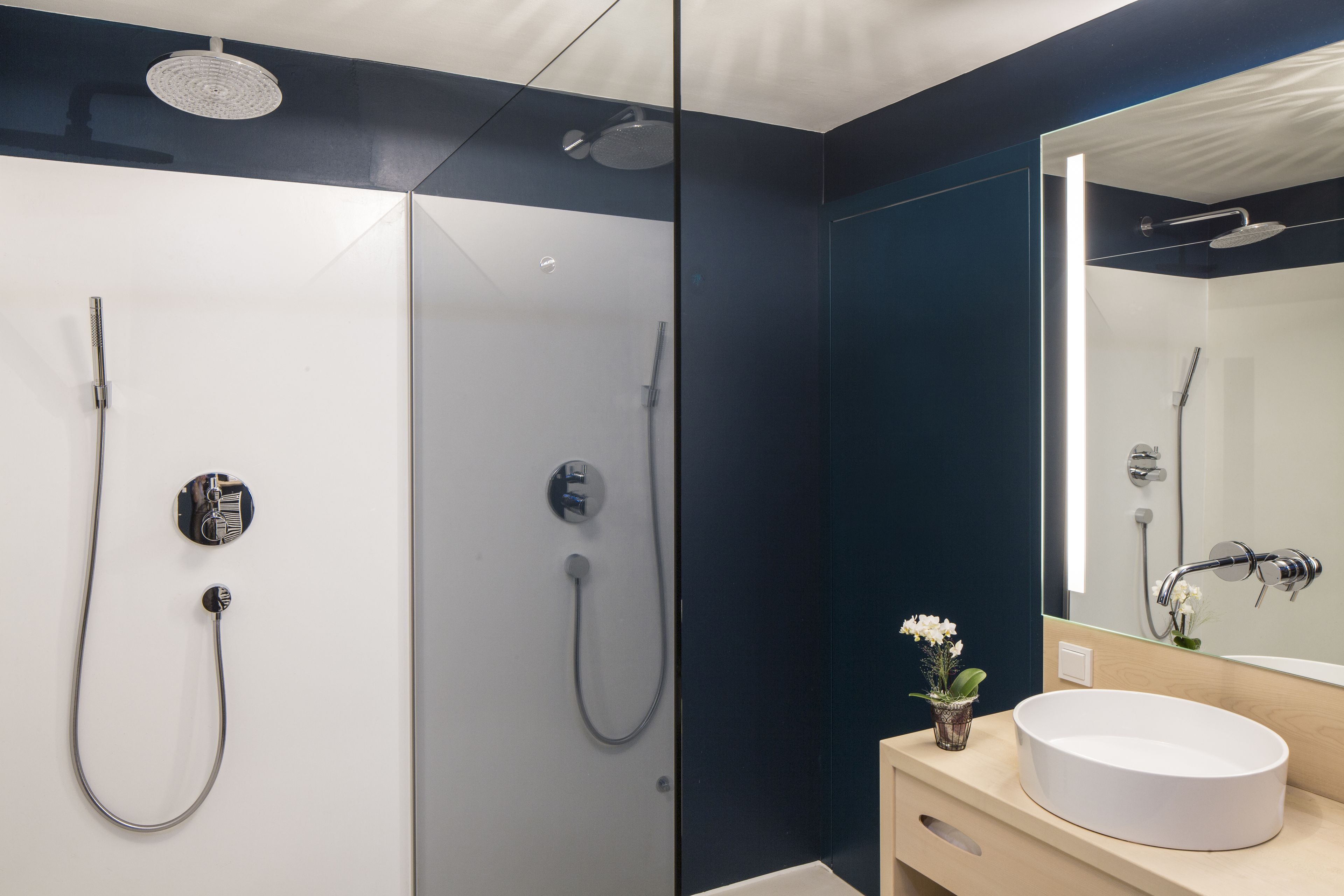 Un baño moderno con un lavabo blanco, un espejo y dos cabezales de ducha.