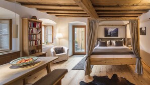 Un dormitorio acogedor con techo de madera, una cama grande con cortinas, una estantería, un escritorio con un frutero y vistas al exterior.