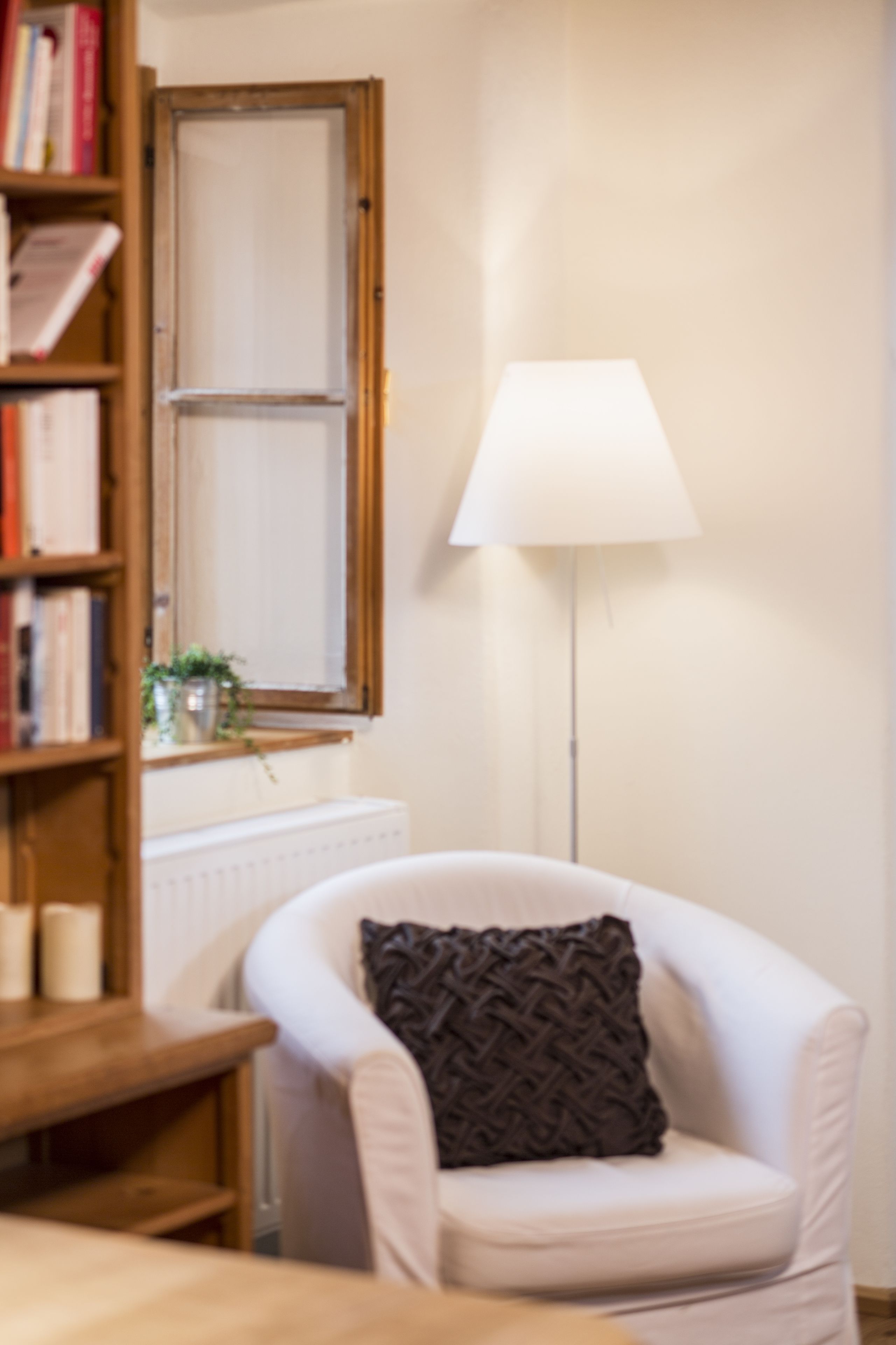 Une pièce avec un fauteuil blanc, un lampadaire, une bibliothèque et un radiateur.
