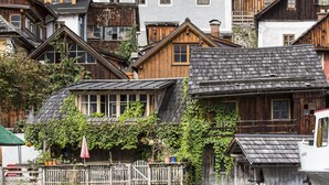 Una casa de madera tradicional con balcón, un edificio blanco con múltiples ventanas y un bote amarrado en el agua.