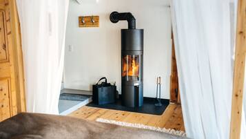 Une pièce chaleureuse avec un poêle à bois, un plancher en bois et un rideau blanc.