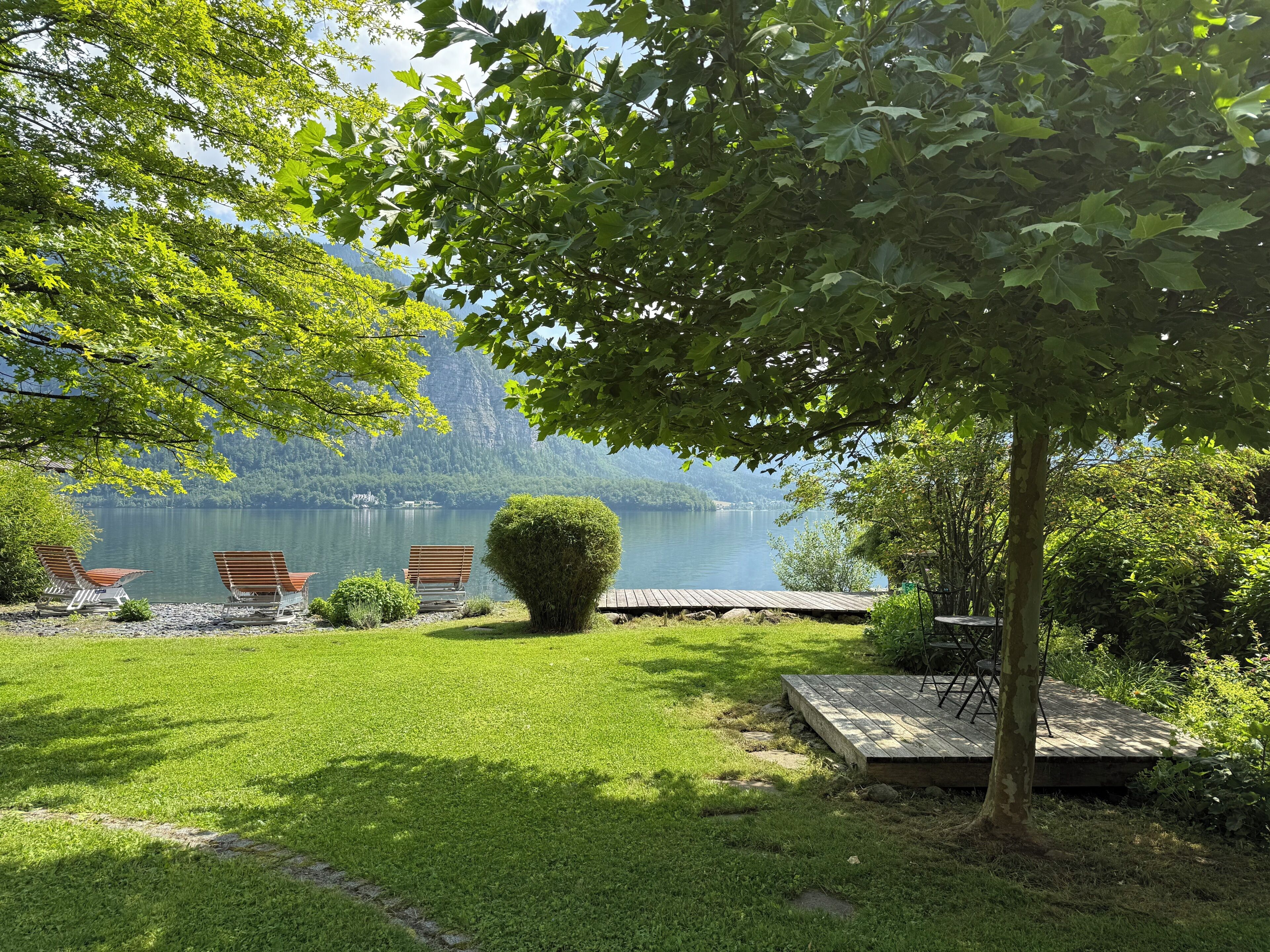 A lakeside garden with a bench, a small stage, and a view of a lake and mountains.