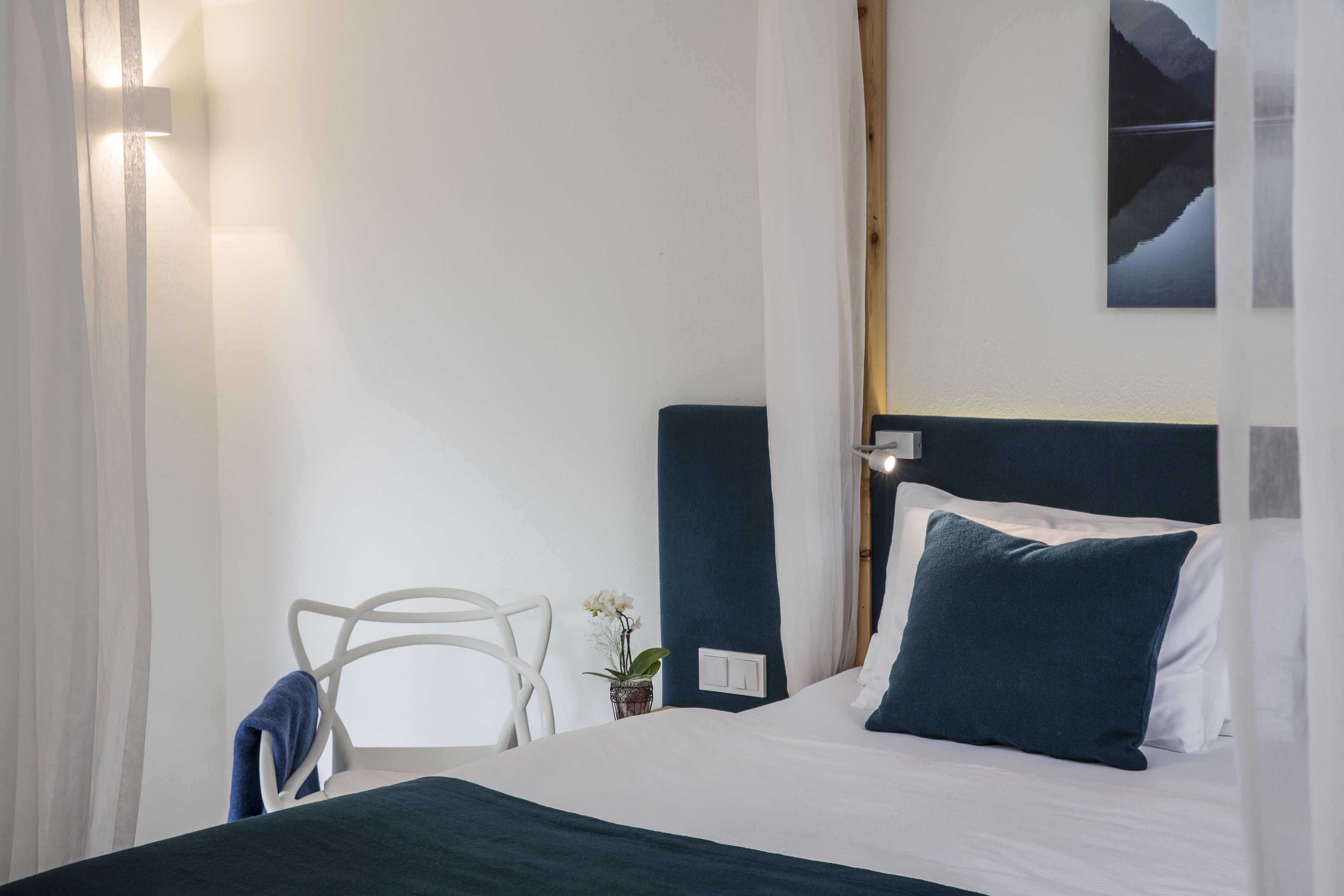 Un dormitorio ordenado con una cama, una silla y una mesita con una planta.